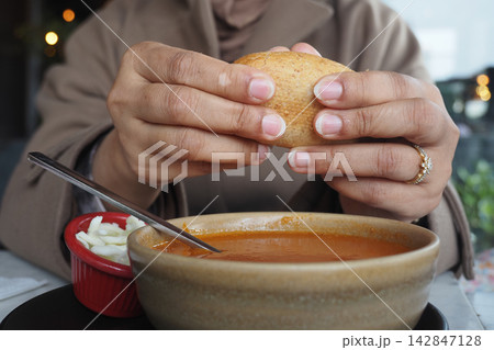 Hands holding bread above a bowl of soup with a side of salad Hands holding bread above a bowl of soup with a side of salad 142847128