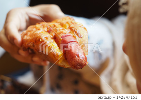 A woman holds a pastry with a hot dog inside while sitting down A woman holds a pastry with a hot dog inside while sitting down 142847153