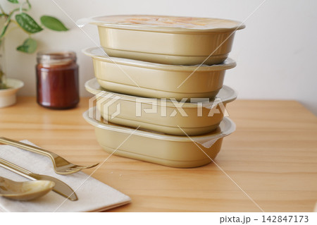 Containers stacked on a wooden table with utensils and a jar nearby Containers stacked on a wooden table with utensils and a jar nearby 142847173