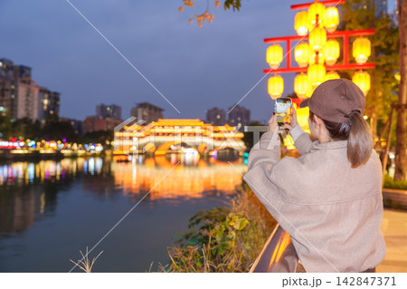 Happy woman traveler travel in Chengdu city. Tourist sightseeing and taking photo to Anshun Bridge by mobile phone at night. Famous Landmark for tourism attraction in Sichuan, China 142847371