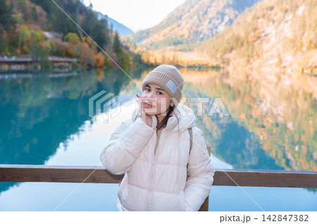 Happy woman traveler travel in jiuzhaigou national park in Sichuan, China. Tourist sightseeing Panda lake and snow mountain in Autumn season. Famous Landmark and Vacation near Chengdu, China 142847382
