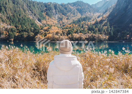Happy woman traveler travel in jiuzhaigou national park in Sichuan, China. Tourist sightseeing Five Flower lake and snow mountain in Autumn season. Famous Landmark and Vacation near Chengdu, China 142847384