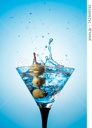 A green olives drops into a martini glass, creating a beautiful splash. A green olives drops into a martini glass, creating a beautiful splash. 142848592