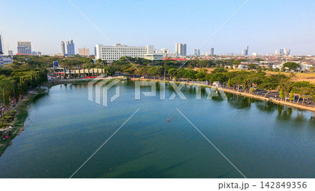 Scenic view of Danau UNESA lake surrounded by green trees and urban skyline in Surabaya, East Java, Indonesia. Scenic view of Danau UNESA lake surrounded by green trees and urban skyline in Surabaya, East Java, Indonesia. 142849356