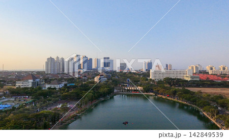 Scenic panoramic view of Danau UNESA lake surrounded by green trees and city skyline in Surabaya, East Java, Indonesia. Scenic panoramic view of Danau UNESA lake surrounded by green trees and city skyline in Surabaya, East Java, Indonesia. 142849539