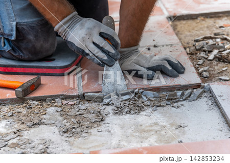 Worker wearing protective gloves cleans the floor base with a scraper after removing old ceramic tiles. 142853234