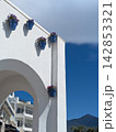 White Mediterranean arch decorated with blue flower pots against a deep blue sky in a traditional Andalusian coastal village with mountain backdrop. Balcon de Europa location. 142853321