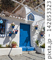 Charming white Mediterranean house with vivid blue door and flower pots nestled beneath rocky cliffs in a picturesque Andalusian coastal settlement 142853323