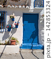 Close up of a vibrant blue wooden door on a whitewashed Andalusian house adorned with colorful flower pots and dramatic sunlit shadows 142853324