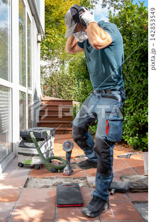 Worker removing ear protection while renovating outdoor patio tiles Worker removing ear protection while renovating outdoor patio tiles 142853549