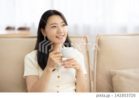 窓辺のソファでコーヒーカップを手にリラックスする若い日本人女性 142853720