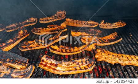 Pork belly strips grilling over open flame with smoky crispy texture 142854428