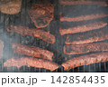 Meat patties and sausage rolls cooking on grill over charcoal. Smoky BBQ scene Meat patties and sausage rolls cooking on grill over charcoal. Smoky BBQ scene 142854435