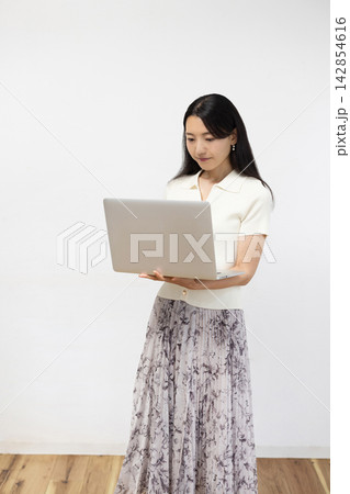 白い壁の前でノートパソコンを操作する若い日本人女性 142854616