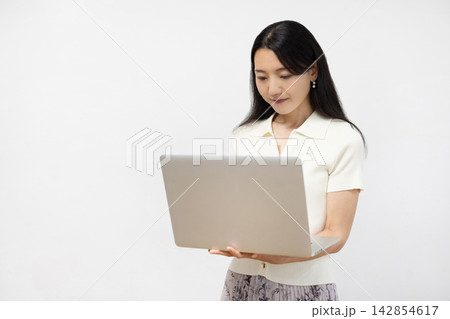 白い壁の前でノートパソコンを操作する若い日本人女性 白い壁の前でノートパソコンを操作する若い日本人女性 142854617