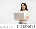 白い壁の前でノートパソコンを持ってカメラ目線で微笑む若い日本人女性 142854618