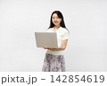 白い壁の前でノートパソコンを持ってカメラ目線で微笑む若い日本人女性 142854619