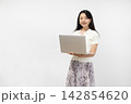 白い壁の前でノートパソコンを持ってカメラ目線で微笑む若い日本人女性 142854620