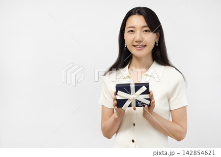 白い壁の前でギフトボックスを持ってカメラ目線で微笑む若い日本人女性 142854621