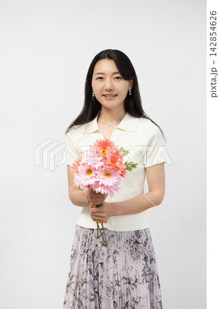 白い壁の前で花束を持ってカメラ目線で微笑む若い日本人女性 白い壁の前で花束を持ってカメラ目線で微笑む若い日本人女性 142854626
