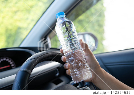 Asian woman driver hold cold water for drink in car, dangerous and risk an accident. 142854635