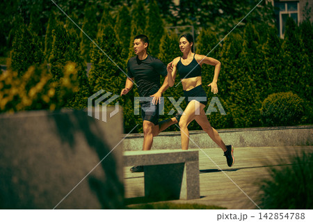 Confident man and woman run together through a green urban park with positive energy 142854788