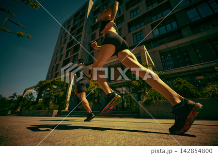 Powerful female and male runners accelerate along a sunny city street with ambition Powerful female and male runners accelerate along a sunny city street with ambition 142854800