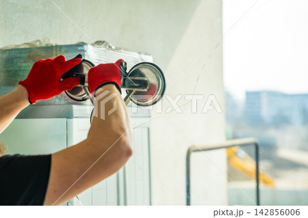 Worker attaching suction cup lifters to cracked window glass before removal from frame during replacement process in apartment. Professional window repair, safe handling, glass installation service 142856006