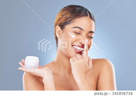 Smile, cream and woman with dermatology, beauty and cosmetics on a blue studio background. Face, person and model with lotion, shine and glow with moisturizer, creme and skincare with aesthetic Smile, cream and woman with dermatology, beauty and cosmetics on a blue studio background. Face, person and model with lotion, shine and glow with moisturizer, creme and skincare with aesthetic 142856738