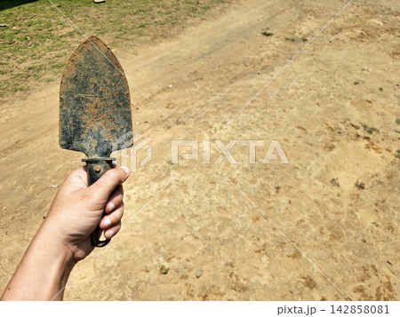 Hand holding small metal trowel tool for gardening outdoors. 142858081