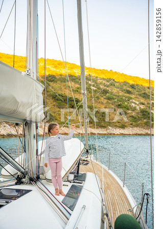 Young girl holding rope on sailing yacht near Croatian coast. Childhood sailing experience encourages practical learning, confidence and connection with the sea 142859156