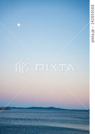Moon rises above calm Adriatic Sea and distant Croatian islands at dusk. Minimal seascape with large copy space represents tranquility and peaceful evening Moon rises above calm Adriatic Sea and distant Croatian islands at dusk. Minimal seascape with large copy space represents tranquility and peaceful evening 142859168