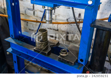 Hydraulic press with metal adapters in auto repair workshop. Garage equipment is used for pressing and removing bearings bushings and vehicle parts Hydraulic press with metal adapters in auto repair workshop. Garage equipment is used for pressing and removing bearings bushings and vehicle parts 142859231
