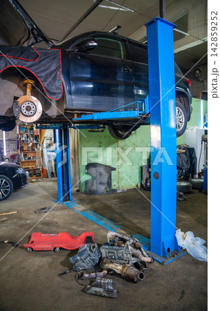 Car raised on hydraulic lift with wheel removed in auto repair shop. Brake inspection and undercarriage service represent vehicle maintenance and repair Car raised on hydraulic lift with wheel removed in auto repair shop. Brake inspection and undercarriage service represent vehicle maintenance and repair 142859252