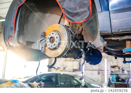 Car raised on hydraulic lift with wheel removed in auto repair shop. Brake inspection and undercarriage service represent vehicle maintenance and repair Car raised on hydraulic lift with wheel removed in auto repair shop. Brake inspection and undercarriage service represent vehicle maintenance and repair 142859256