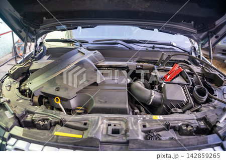 Jumper cable connected to car battery under open hood. Jump starting vehicle represents battery failure, roadside repair and automotive maintenance Jumper cable connected to car battery under open hood. Jump starting vehicle represents battery failure, roadside repair and automotive maintenance 142859265