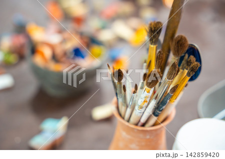Paintbrushes for glazing and decorating ceramics stand on pottery workshop table. Ceramic tools represent craftsmanship and handmade pottery creation 142859420