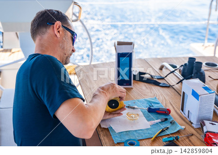 Man repairing yacht equipment with hand tools during a sailing trip on the Adriatic Sea. Concept of boat maintenance, DIY repair, seamanship, technical skills and self-sufficient sailing. Man repairing yacht equipment with hand tools during a sailing trip on the Adriatic Sea. Concept of boat maintenance, DIY repair, seamanship, technical skills and self-sufficient sailing. 142859804