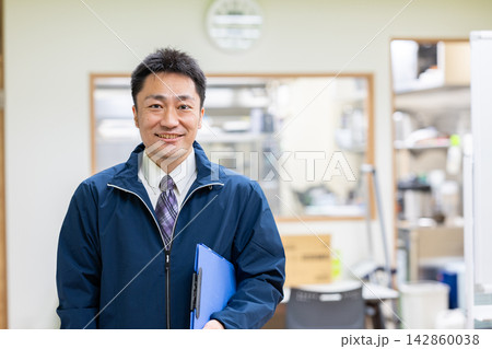 厨房でクリップボードを手に笑顔で点検を行う作業服の男性 142860038
