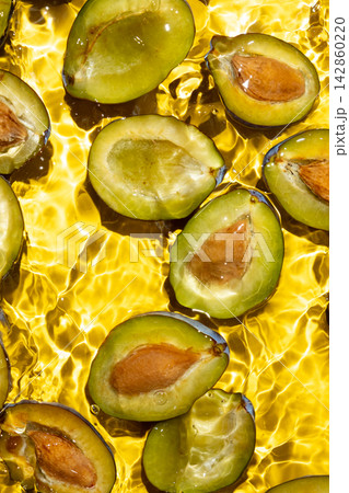Halved ripe plums with seeds submerged in clear splashing water top view Halved ripe plums with seeds submerged in clear splashing water top view 142860220