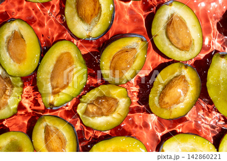 Fresh plum halves with pits floating in clean water overhead view 142860221