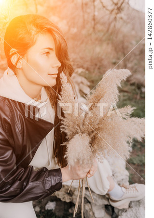 Woman pampas portrait young woman in leather jacket holding dried grass bouquet sitting in nature during golden hour Woman pampas portrait young woman in leather jacket holding dried grass bouquet sitting in nature during golden hour 142860377