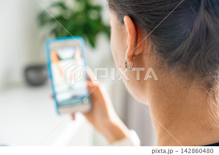 Woman scrolling social media on a smartphone at home. Digital addiction concept with endless content consumption and screen time. Woman scrolling social media on a smartphone at home. Digital addiction concept with endless content consumption and screen time. 142860480