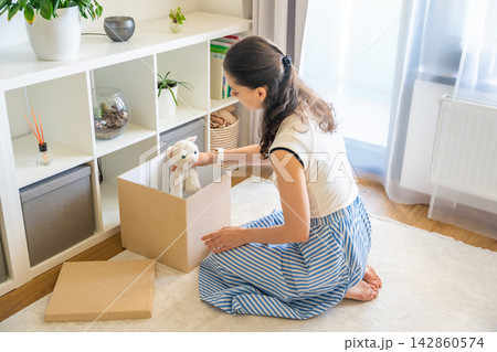 Young woman taking old stuffed toy from storage box in home interior. Home organization and decluttering with childhood memories concept Young woman taking old stuffed toy from storage box in home interior. Home organization and decluttering with childhood memories concept 142860574