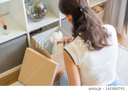 Young woman taking old stuffed toy from storage box in home interior. Home organization and decluttering with childhood memories concept 142860741