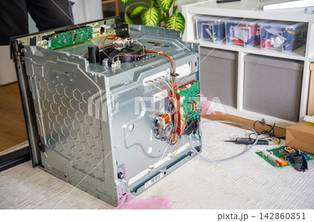Home appliance repair workspace with disassembled electric oven and replacement electronic parts. Professional service concept 142860851