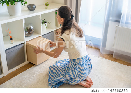 Young woman pulling storage box from shelving system in home interior. Home organization and decluttering routine concept Young woman pulling storage box from shelving system in home interior. Home organization and decluttering routine concept 142860873