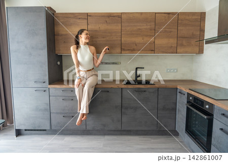 Young woman sitting on kitchen counter in modern apartment and holding house keys. Female home ownership and independent property investment concept 142861007