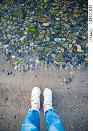 Person standing near transparent sea water with colorful stones on Ruegen island beach in Germany. Travel, relaxation and clean Baltic Sea coastline 142861043
