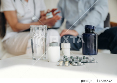 Medical consultation scene with healthcare professional discussing medication options with patient, various pill bottles and a glass of water on the table Medical consultation scene with healthcare professional discussing medication options with patient, various pill bottles and a glass of water on the table 142862321